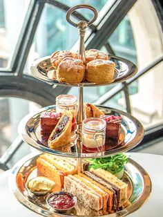 three tiered tray with sandwiches and jams on it in front of a window