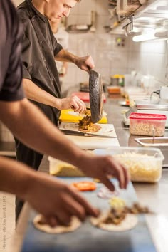 two men in a kitchen preparing food on top of a cutting board with utensils