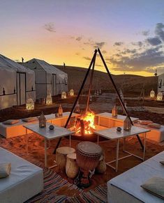 an outdoor fire pit surrounded by white tables and chairs with lit candles on them at sunset