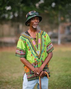 an old man standing in the grass holding a cane and wearing a colorful shirt with flowers on it