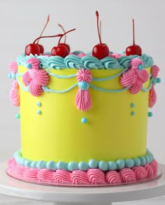 a yellow cake with pink, blue and green frosting topped with two cherries