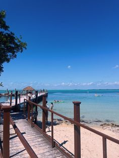 a wooden walkway leading to the beach with boats in the water and people walking on it