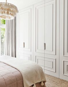 a bedroom with white closets and beige bedding, along with a chandelier hanging from the ceiling