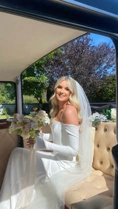 a woman in a wedding dress sitting on a car