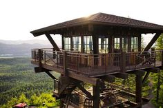 a tall wooden structure sitting on top of a lush green hillside next to a forest