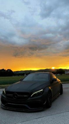 a black car parked in front of a field with the sun going down behind it