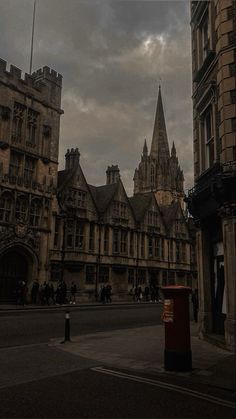 an old castle like building with people walking in the street below it on a cloudy day