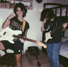 two people standing in a room with guitars and one person holding a guitar up to his ear