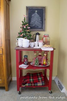 a red cart with christmas decorations on it in front of a painting and coffee mugs