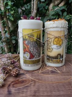 two candles sitting next to each other on top of a wooden table in front of trees