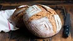 two loaves of bread sitting on top of a wooden table next to a knife