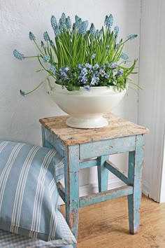 a white bowl filled with blue flowers sitting on top of a wooden table next to a pillow