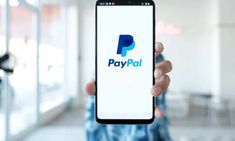 a person holding up a cell phone with the paypal logo on it in front of them