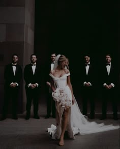 a woman in a wedding dress standing next to a group of men wearing tuxedos