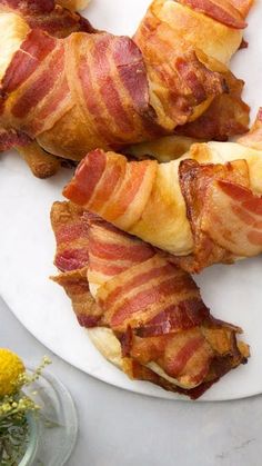 bacon wrapped in strips on a white plate next to yellow flowers and a glass vase