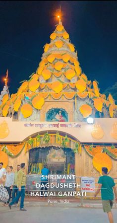 people are standing in front of a yellow and white building with orange decorations on it