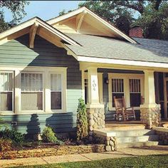 a small blue house with white trim on the front door and porch, sitting next to a tree