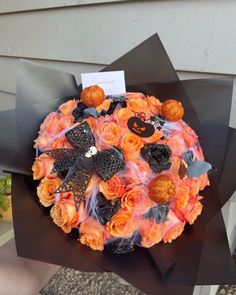 a bouquet of orange roses with black and white decorations on it, in front of a house