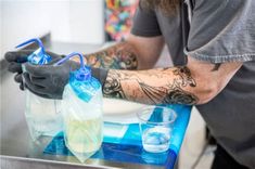 a man with tattoos on his arm and arms is filling up water bottles onto a table