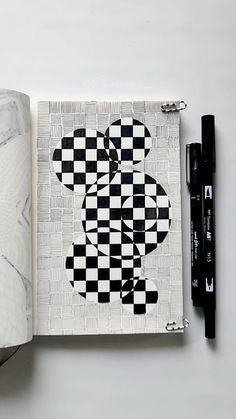 an open notebook with a black and white checkered teddy bear on the cover next to a pen