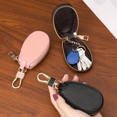 a hand holding a key chain with two small purses attached to it on top of a wooden table