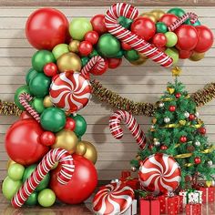 a christmas balloon arch decorated with candy canes and ornaments next to a christmas tree