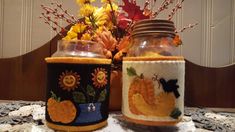 two jars with pumpkins and flowers in them on a doily covered tablecloth