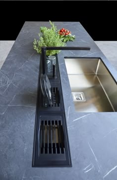 a sink and drain in a kitchen with grey marble counter tops, stainless steel sinks and black grates on the floor