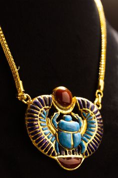 a gold necklace with an egyptian scarabra and red stone in the center on a black mannequin