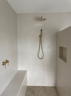 an empty bathroom with a shower head and white walls, along with herringbone tile flooring