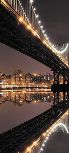 the bridge is lit up at night and reflecting in the water