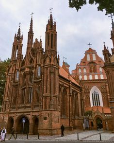 an old church with two towers and people walking by it on the street in front of it