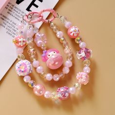 a pink necklace with charms and beads on top of a table next to a book