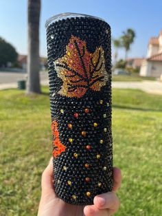 a hand holding up a black and orange beaded coffee cup in front of a palm tree