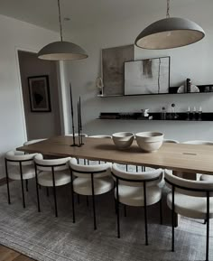 a dining room table with six chairs and bowls on the top, in front of hanging lights