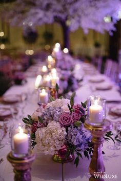 a long table with purple and white flowers on it is set for a formal dinner