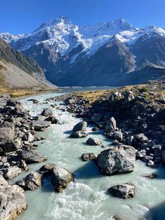 a river running through the middle of a mountain range with snow covered mountains in the background