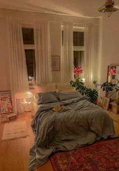 a bed sitting in a bedroom next to a window filled with curtains and pillows on top of a wooden floor