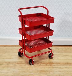 a red three - tiered cart with wheels sits on the floor in front of a wall