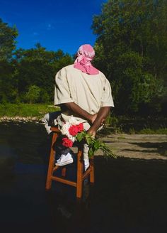 a man sitting on a chair with flowers in his lap and wearing a pink scarf