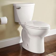 a white toilet sitting on top of a hard wood floor next to a roll of toilet paper