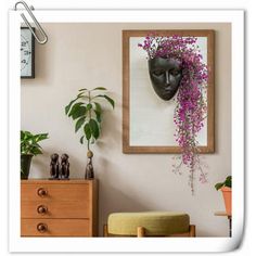 a vase with purple flowers hanging from it's side in front of a painting on the wall