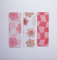 three bookmarks with flowers and smiley faces are lined up against a white background,