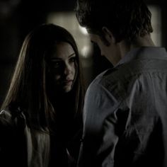 two people standing in the dark looking at each other and one person has her hand on his shoulder