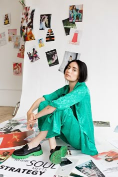 a woman sitting on the ground surrounded by pictures and posters, with her hands in her pockets