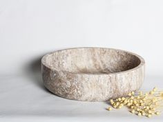 a wooden bowl sitting on top of a white table next to some yellow flowers in front of it