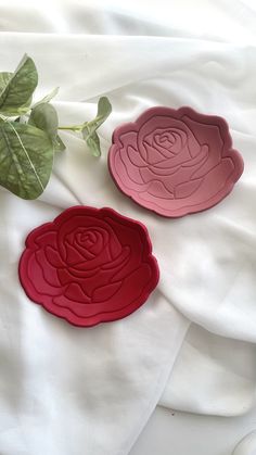 two red and pink flower shaped plates sitting on top of a white cloth covered bed