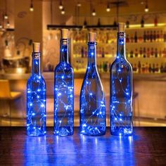 three bottles with lights in them sitting on a table next to a bar and shelves