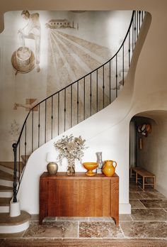 a staircase in a home with vases on the table and paintings on the wall