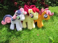 crocheted little ponys lined up on the grass in front of some bushes